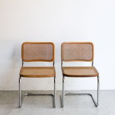 two brown chairs sitting next to each other on a cement floor in front of a white wall