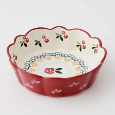 a red and white bowl with cherries on the rim is sitting in front of a white background