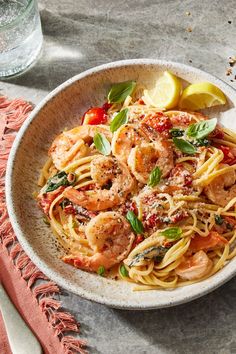 a white bowl filled with pasta and shrimp on top of a table next to a glass of water