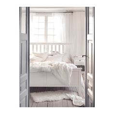 a white bed sitting in a bedroom next to an open door with curtains on it