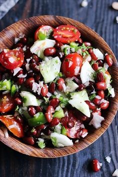 a wooden bowl filled with beans and cucumber on top of a black table