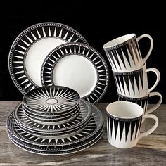 a stack of black and white plates, cups and saucers on a wooden table