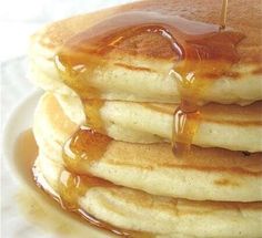 stack of pancakes covered in syrup on top of a white plate with honey drizzled over them