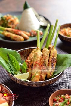 some food in bowls on a table with green leaves and other foods around it,