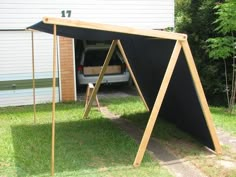 a black awning sitting in the grass next to a white car and building with trees behind it