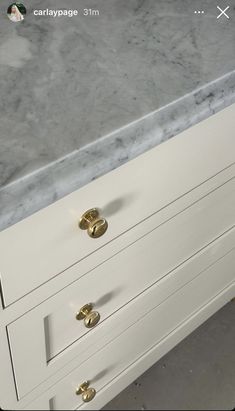 a white dresser with gold handles and marble top