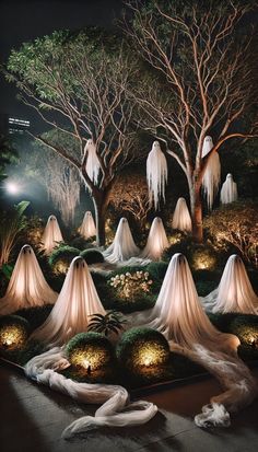 an outdoor display with white cloth draped around trees and lights on the ground in front of them