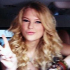 a woman sitting in the back seat of a car making a peace sign with her fingers