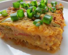 a white plate topped with a piece of food covered in cheese and green onion slices