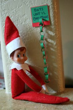 an elf is sitting on the floor next to a sign that says days until christmas