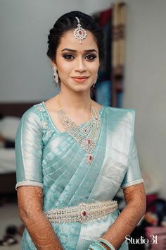 a woman in a blue sari with jewelry on her neck and hands behind her back