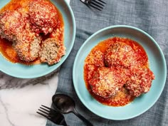 two blue plates filled with meatballs covered in marinara sauce and parmesan cheese