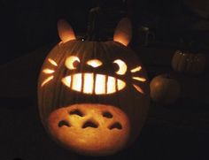 a pumpkin carved to look like a cat with glowing eyes and mouth, is lit up in the dark