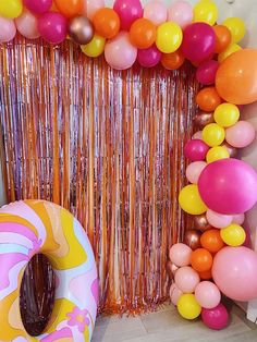 balloons and streamers are hanging from the wall behind a balloon arch with a donut