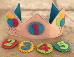 a pink felt crown with numbers and balloons on the front, sitting on a stone surface