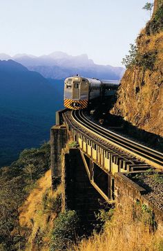 a train traveling over a bridge on top of a mountain with mountains in the background