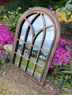 a mirror sitting on the ground in front of some purple and yellow flowers with pink flowers behind it