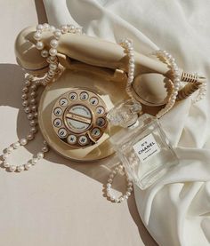 an old fashioned telephone and pearls on a white sheet with a bottle of perfume next to it