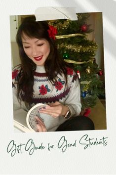 a woman sitting in front of a christmas tree holding a book and looking at her cell phone