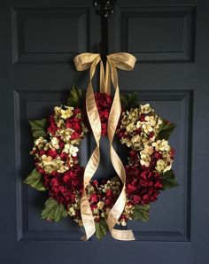 a wreath is hanging on the front door with gold ribbon and red flowers in it