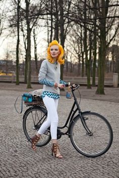 a woman is standing next to her bike in the middle of an open area with trees