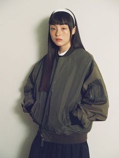 a young woman standing in front of a white wall wearing a green jacket and black skirt