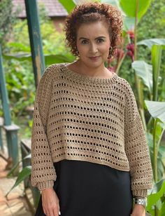 a woman wearing a brown crochet sweater standing in front of some green plants