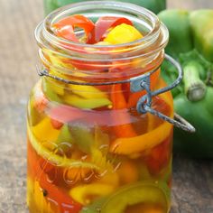 a jar filled with pickles sitting on top of a wooden table next to green peppers