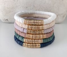 five different colored bracelets stacked on top of each other with gold and white beads