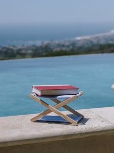 a stack of books sitting on top of a wooden chair next to the ocean and mountains