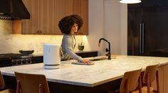 a woman standing at a kitchen counter with an appliance in front of her