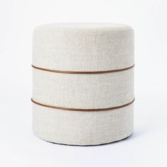 a white round ottoman with two brown stripes on the bottom and one stripe down the middle