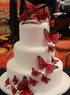 a three tiered white cake with red butterflies on it