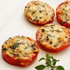 four stuffed tomatoes with cheese and herbs sitting on a white surface next to a plant