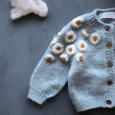 a blue sweater with white flowers on it and a teddy bear laying next to it