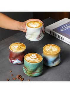 three coffee mugs with designs on them sitting on a table next to some coffee beans