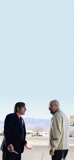 two men in business suits are talking to each other on the tarmac with a kite flying overhead