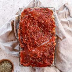 meatloaf covered in marinara sauce on a wire rack next to a bowl of seasoning