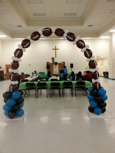 an arch made out of balloons and footballs on the floor in a school hall