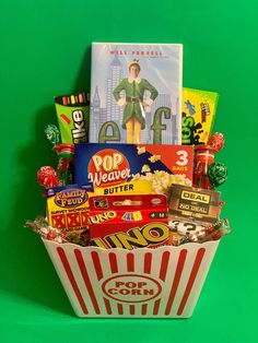 a popcorn bucket filled with snacks and candy on top of a green background, next to a movie poster