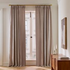 a living room with a large window covered in curtains next to a wooden table and dresser