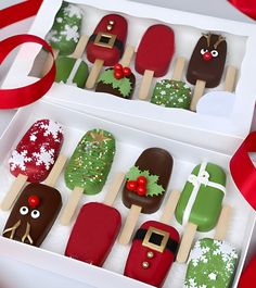 two boxes filled with christmas themed popsicles on top of snow covered ground next to a red ribbon