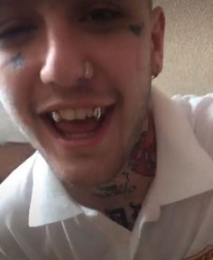 a man with piercings on his face and nose smiles at the camera while wearing a white shirt