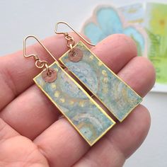 a pair of gold earrings with blue and white designs on them in the palm of a person's hand