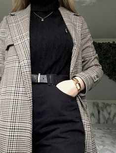 a woman wearing a black turtle neck sweater and checkered blazer jacket with her hands in her pockets