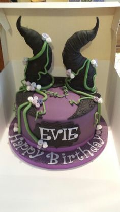 a purple and black cake with horns on top in a white box that says evie happy birthday