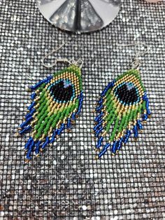 a pair of beaded peacock earrings sitting on top of a table