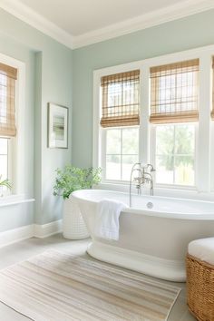 a white bath tub sitting in a bathroom next to two windows and a rug on the floor