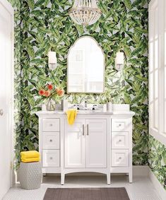 a bathroom with green leaves on the wall and a white vanity, mirror, and yellow towels