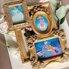 three disney princess paintings are on display in ornate gold frames with pink flowers behind them